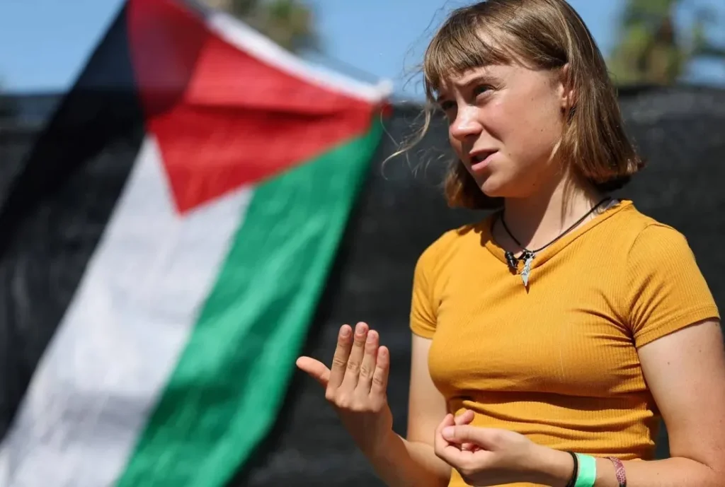 الناشطة السويدية غريتا تونبرغ عضوة اللجنة التوجيهية في «أسطول الصمود العالمي» تتحدث للإعلام ببرشلونة وخلفها علم فلسطين (أرشيفية - أ.ف.ب)